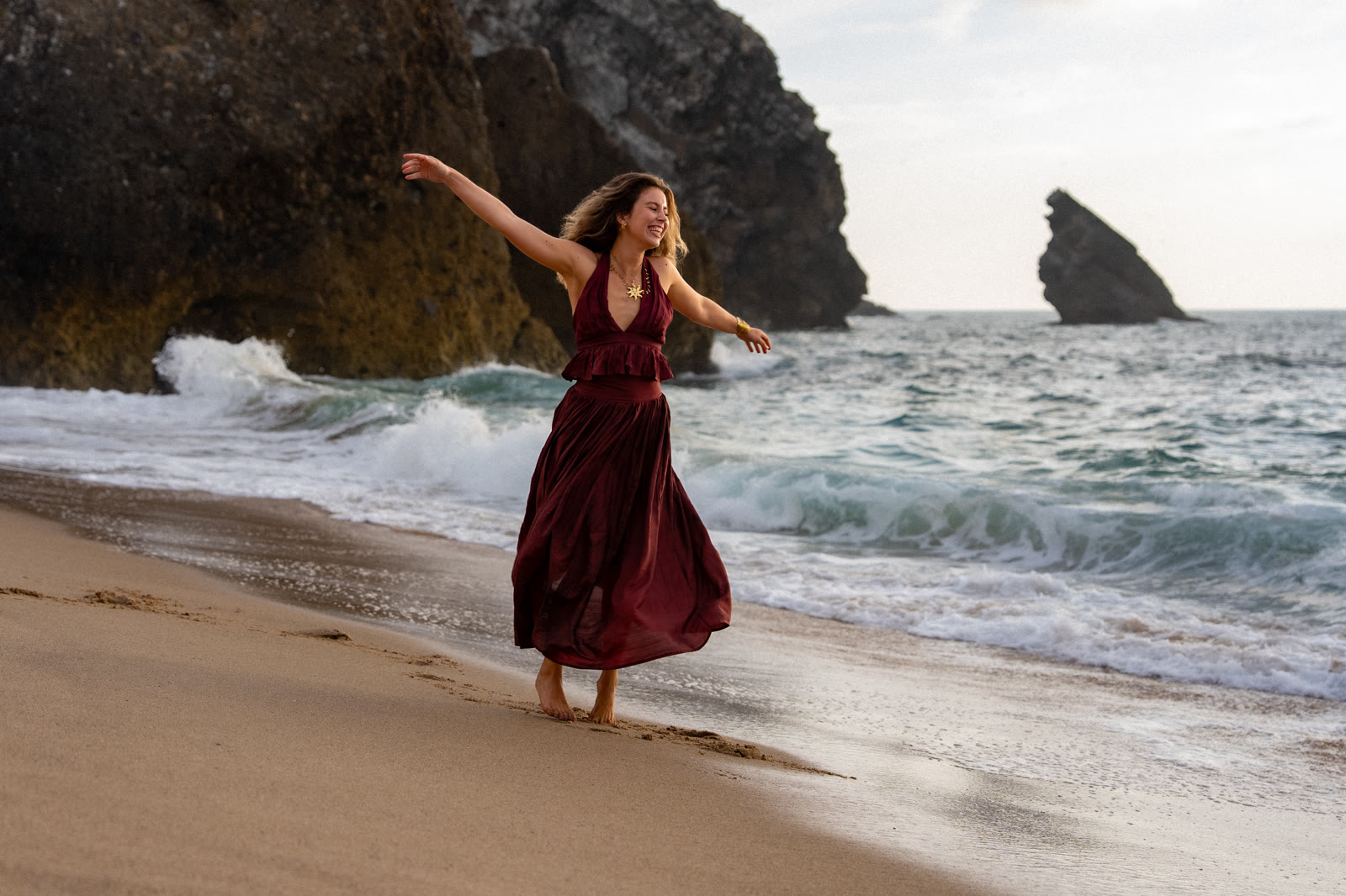 Woman in a red dress dancing on the beach by the rocks