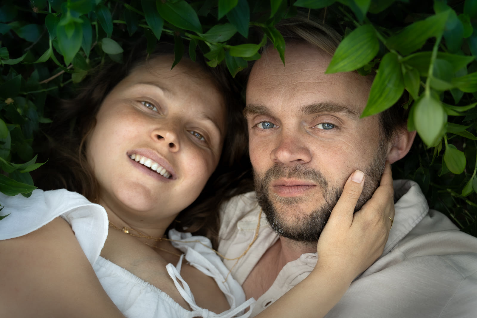 Couple lying close together beneath green leaves