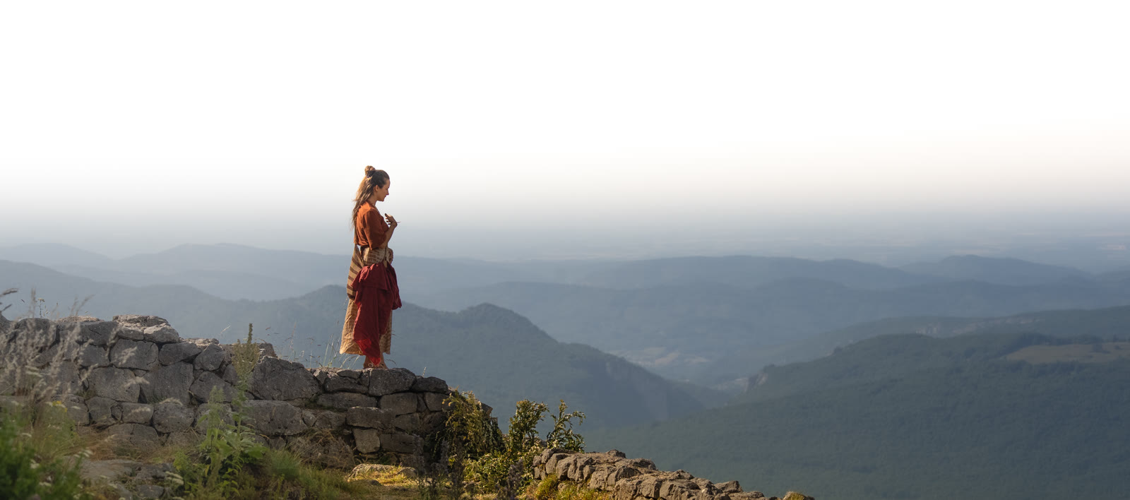 Woman standing on a rocky ledge above misty mountains