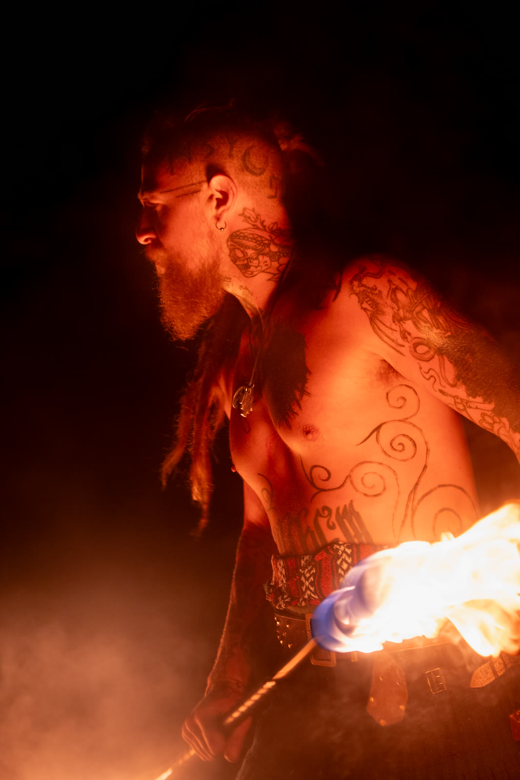 Fire performer with painted skin lit by a flaming torch at night
