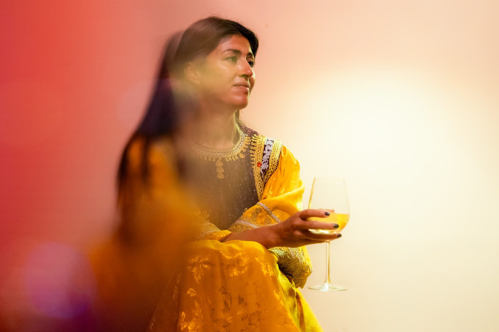 Woman in a yellow embroidered dress holding a glass, in warm coloured light